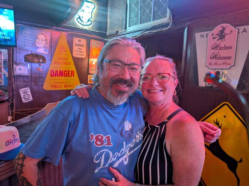 A man with glasses and a goatee hugging a woman with glasses at a bar.