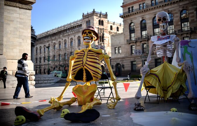A man passes next to fake giant skeletons placed in an altar in front of the Fine Arts Palace for Day of the Dead in Mexico City on November 1, 2016.