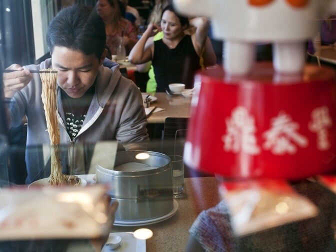Justin Quan eats a noodle dish during lunch with his mother. At right, the Chinese charters for "Din Tai Fung."