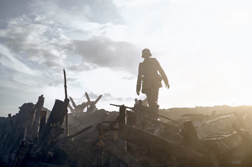 A silhouetted soldier can be seen atop rubble and trenches in daylight during WWI.