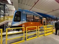 A blue and orange streetcar behind yellow barriers.