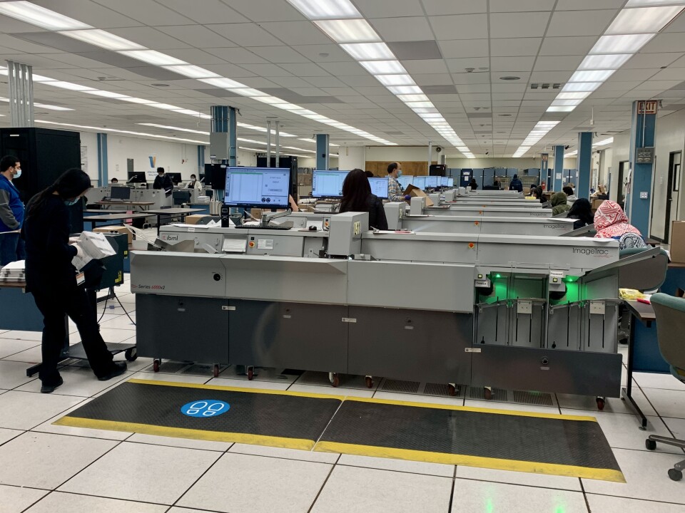 Workers stand by several rows of giant scanners more than 10 feet long.