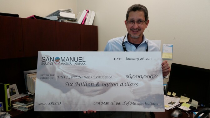 Alfredo Cruz, general manager of FNX and KVCR holds a check from the San Manuel Board of Mission Indians. The funds will support three years of programming and operations