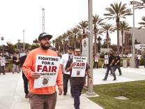 Men walk in front of county buildings holding signs that say, "Fighting for a fair contract." 