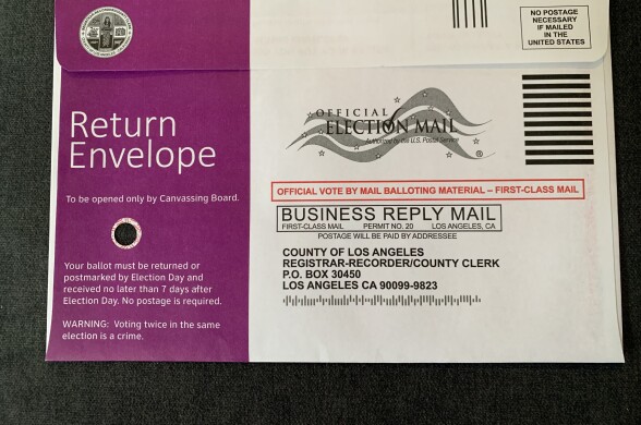 A close-up image of a return envelope for a mail-in ballot. The left side is purple and reads "Return Envelope" in large text. There is a small hole underneath that text.