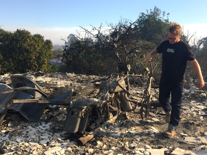 Chris Cairns carries his grandson's bicycle out of the ashes of his garage on Foothill Rd in Ventura.