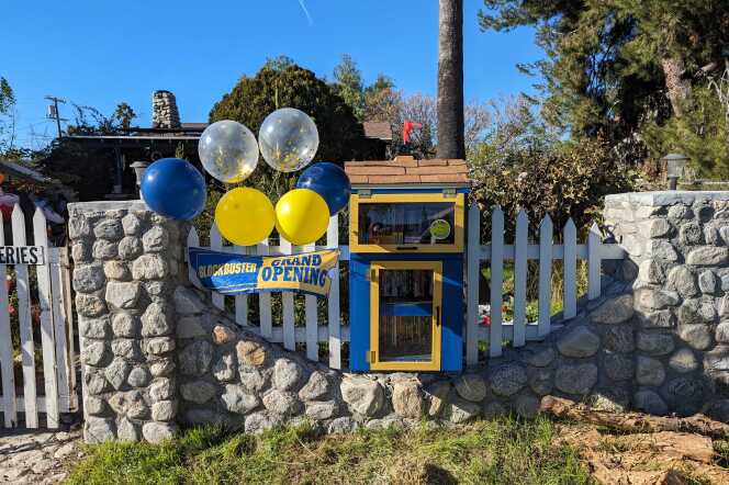 A wooden box painted in blue and yellow built along a picket fence in front of a house.