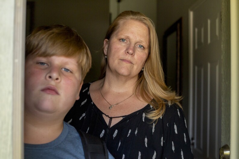 A woman and young boy stand in the doorway of a home. Both have light hair and blue eyes.