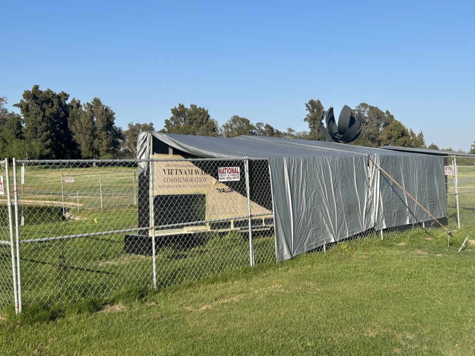 A sign reading Vietnam War commemoration is visible behond a chainlink fence. the structure is draped in silver tarps.