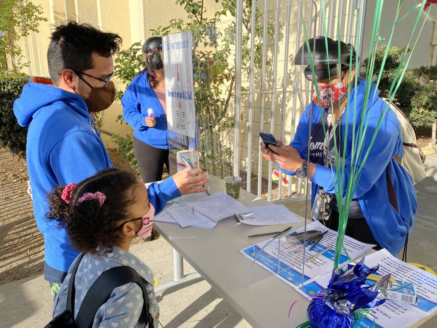 A staffer at the front entrance of Cienega Elementary in West Adams checks a student's Daily Pass — the online QR code created through an L.A. Unified School District app that allows students access to campus — on April 15, 2021.