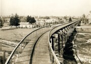 A black and white view of the California Cyclceway looking north from Raymond Hotel. The Santa Fe tracks are below and Fair Oaks Avenue is on left side. The cycleway is a wooden elevated path that curves as it extends away from the camera.