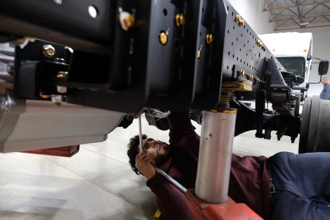 A young man works under the chassi of a truck. 