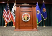 A wooden podium is placed in front of four flags. The podium has a sign that reads "District Attorney, County of Los Angeles".