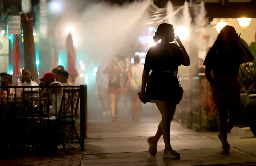 Two women walk in silhouette as water misters cool down diners in a restaurant in Palm Springs.