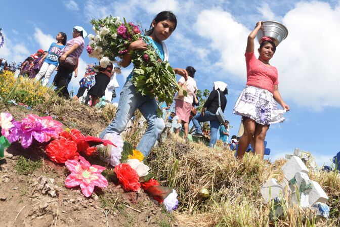 A girl takes flowers to the grave of a loved one during the commemoration of the day of the dead at a cemetery in Panchimalco, El Salvador on November 2, 2016.