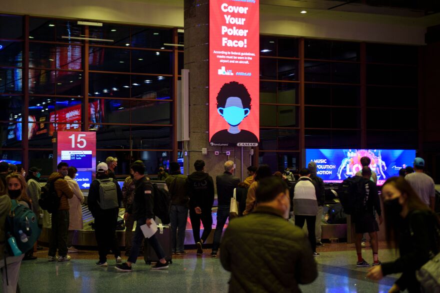 A red lighted sign hangs about a full story tall in an airport terminal and reads: "Cover Your Poker Face!" with the image of a masked person.