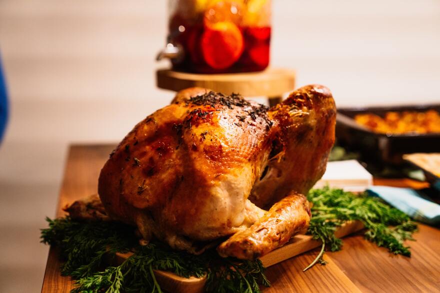 An image of a roasted turkey sitting on a wooden table with greens beneath it.