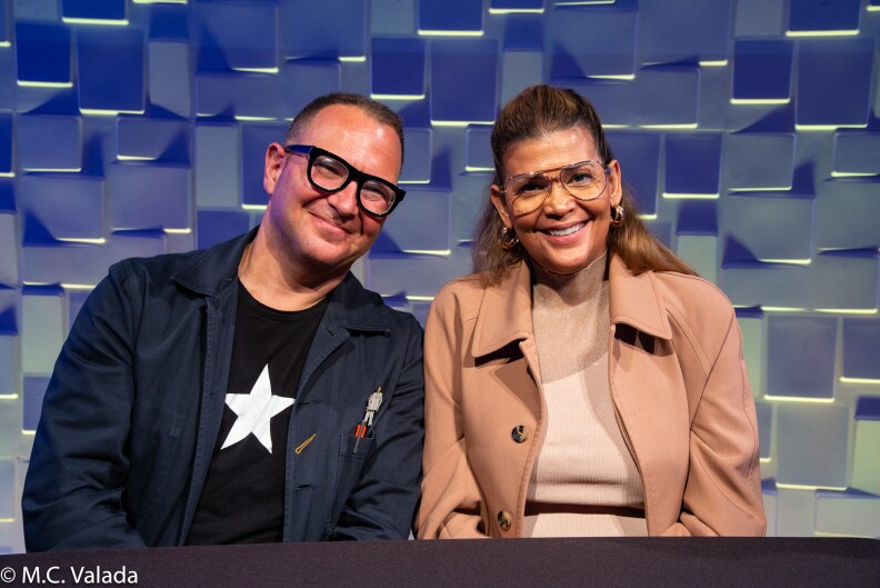 Cory Doctorow, a white man with glasses and Aida Rodriguez, a Hispanic woman with glasses, smiling at the camera at the panelist table