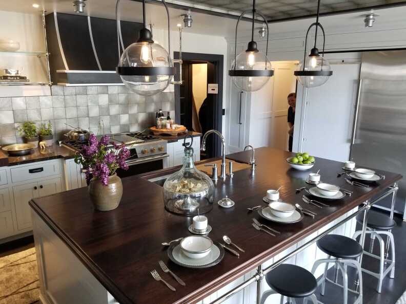 Barstools at a wood-topped kitchen island with dinner and flatware siting on top.