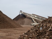 An image featuring mounds of compost, a pile of green waste in the foreground. A large crane dumps compost onto a pile in the background. 