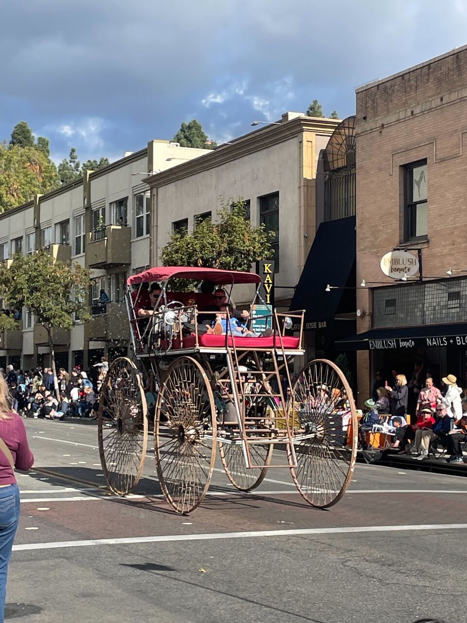 A carriage-style vehicle with massive wheels on a parade route.