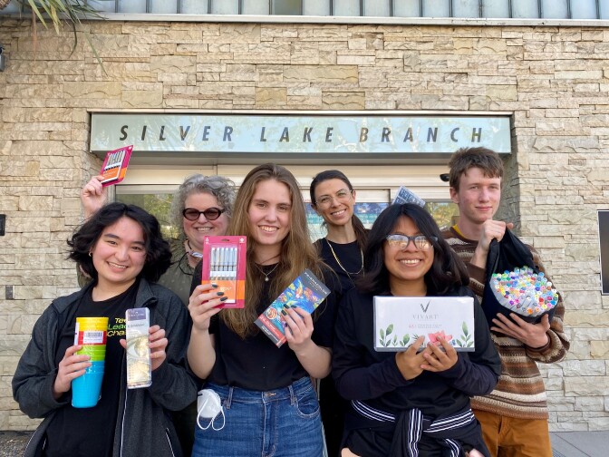 Four teenagers and two librarians stand in front of the Silverlake Branch Library holding art supplies.