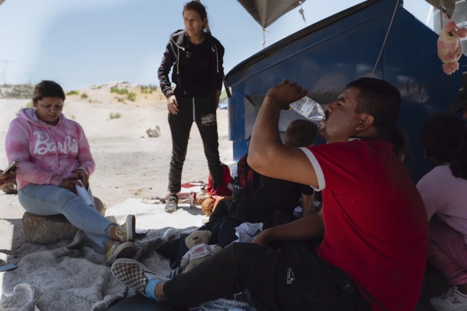 Two groups of people try to stay cool under a shade structure while drinking water 