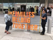 Demonstrators Peta Orbach and Brian Aguilar hold a sign in front of the ICE building in downtown LA while dozens line up outside to support one young father facing deportation.