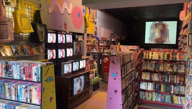A view inside Whammy Analog Video. Countless VHS tapes can be seen lining the walls. A large projected screen is in the background. A row of old CRT Televisions sit on the left side of the picture.