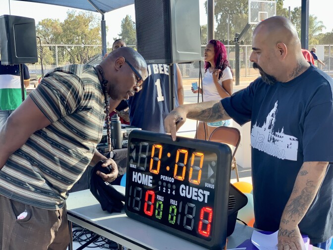 Two men stand around a rectangular table with a small electronic scoreboard on top of it.