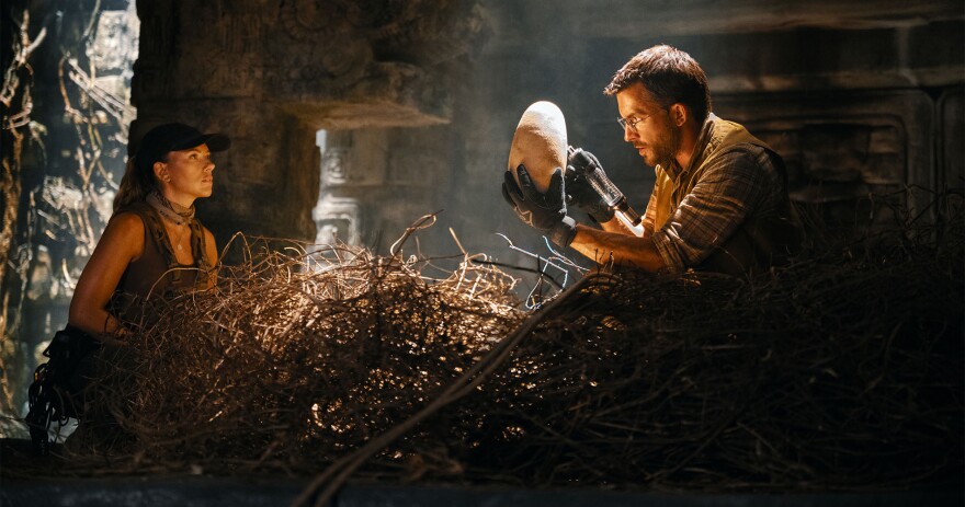 Two people in a cave, examining a dinosaur's egg