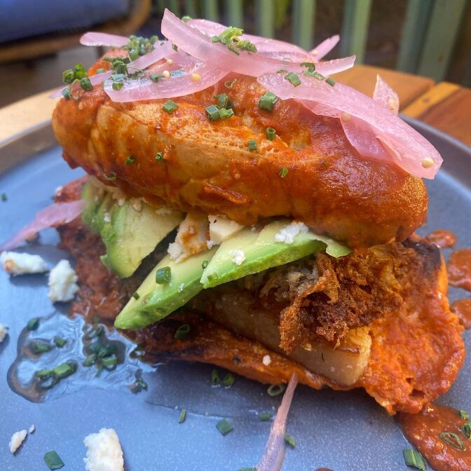 A torta mojada with avocado, red sauce, and pickled onions on top is set on a blue plate.
