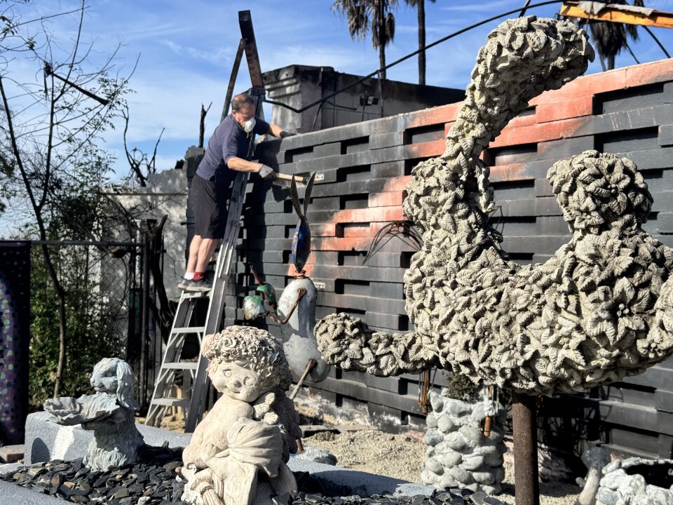 Bunny figures at the front of the photo, as a man with a face mask cleans debris off a wall outdoors.