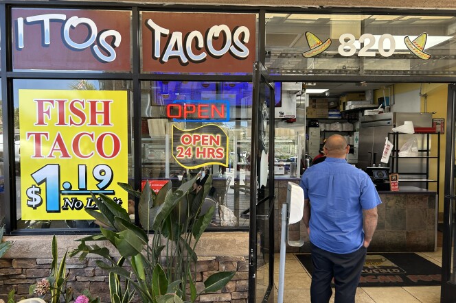 A man in a blue shirt stands in the doorway next to a sign that says "Fish tacos $1.19, No Limit."