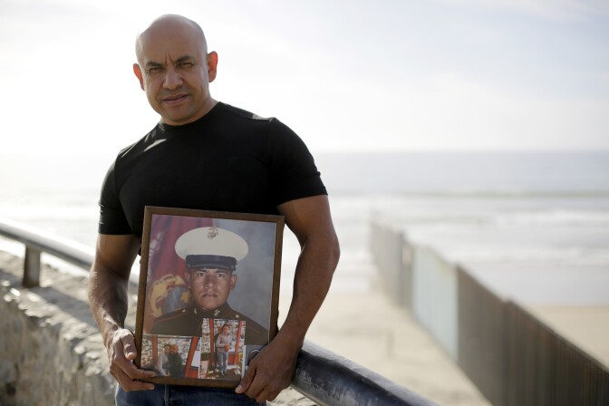 U.S. Marine Corps veteran Antonio Romo on Feb. 13, 2017, holds a picture of himself taken from his days at boot camp, as he poses for a portrait next to the U.S. border wall on the beach in Tijuana, Mexico. Romo is part of a group of dozens of U.S. military veterans who were deported after criminal convictions and for years have fought to be allowed to return.