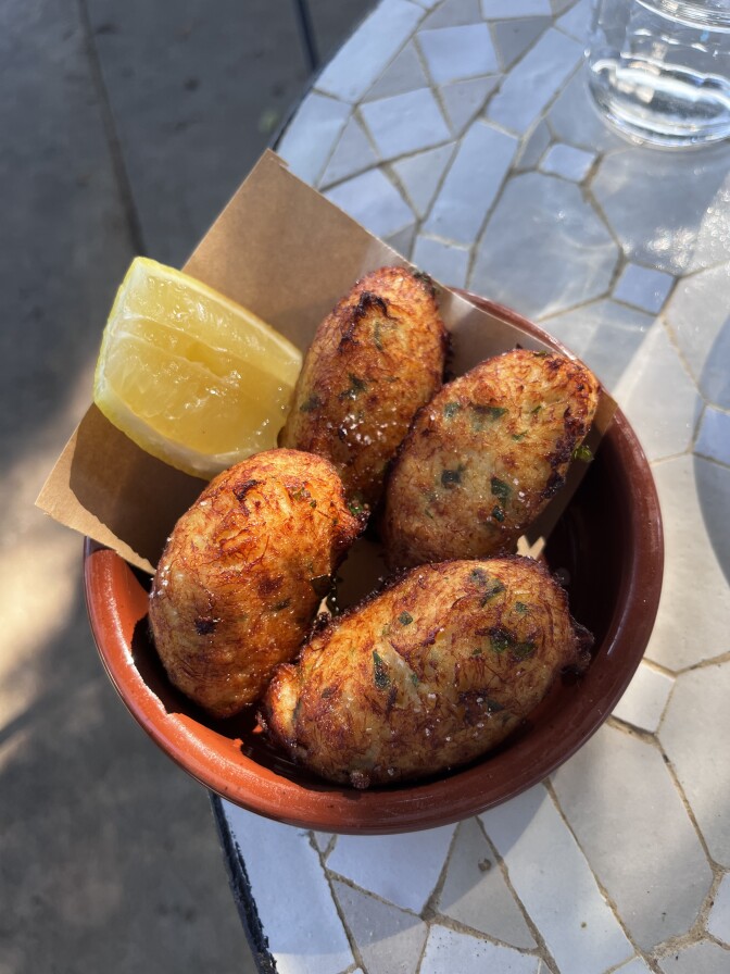 An overhead shot of salted cod fritters in a ceramic dish with yellow lemon wedge 