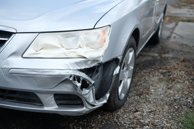 A closeup of the melted bumper of a silver small car. 