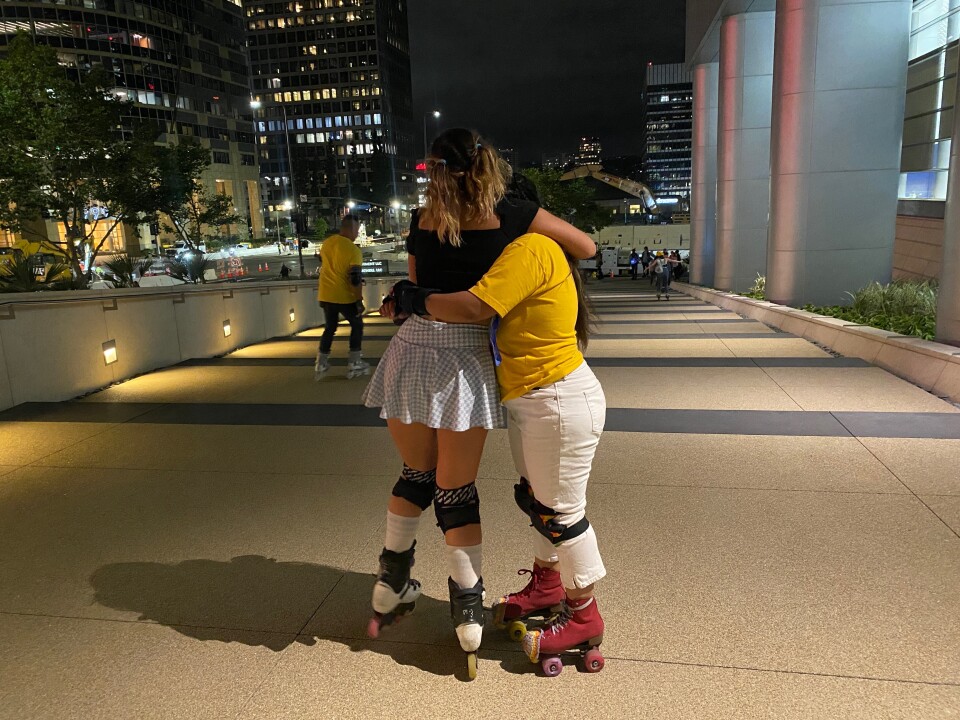 Two people in skates hug on a walkway at night.