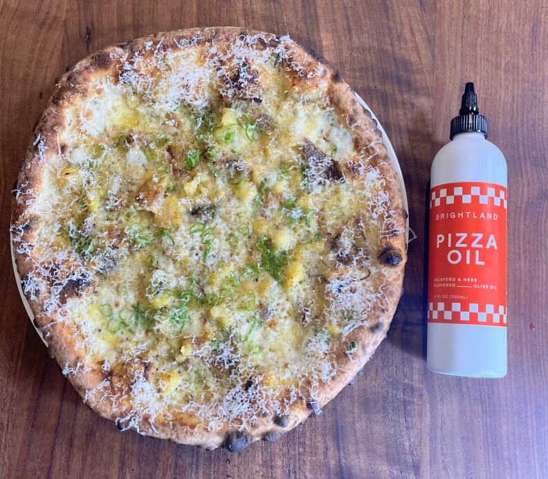 A Neapolitan-style pizza with Root's potatoes, Cowgirl Creamery Wagon Wheel cheese and more, laid on a wooden table next to a bottle of Brightland pizza oil.