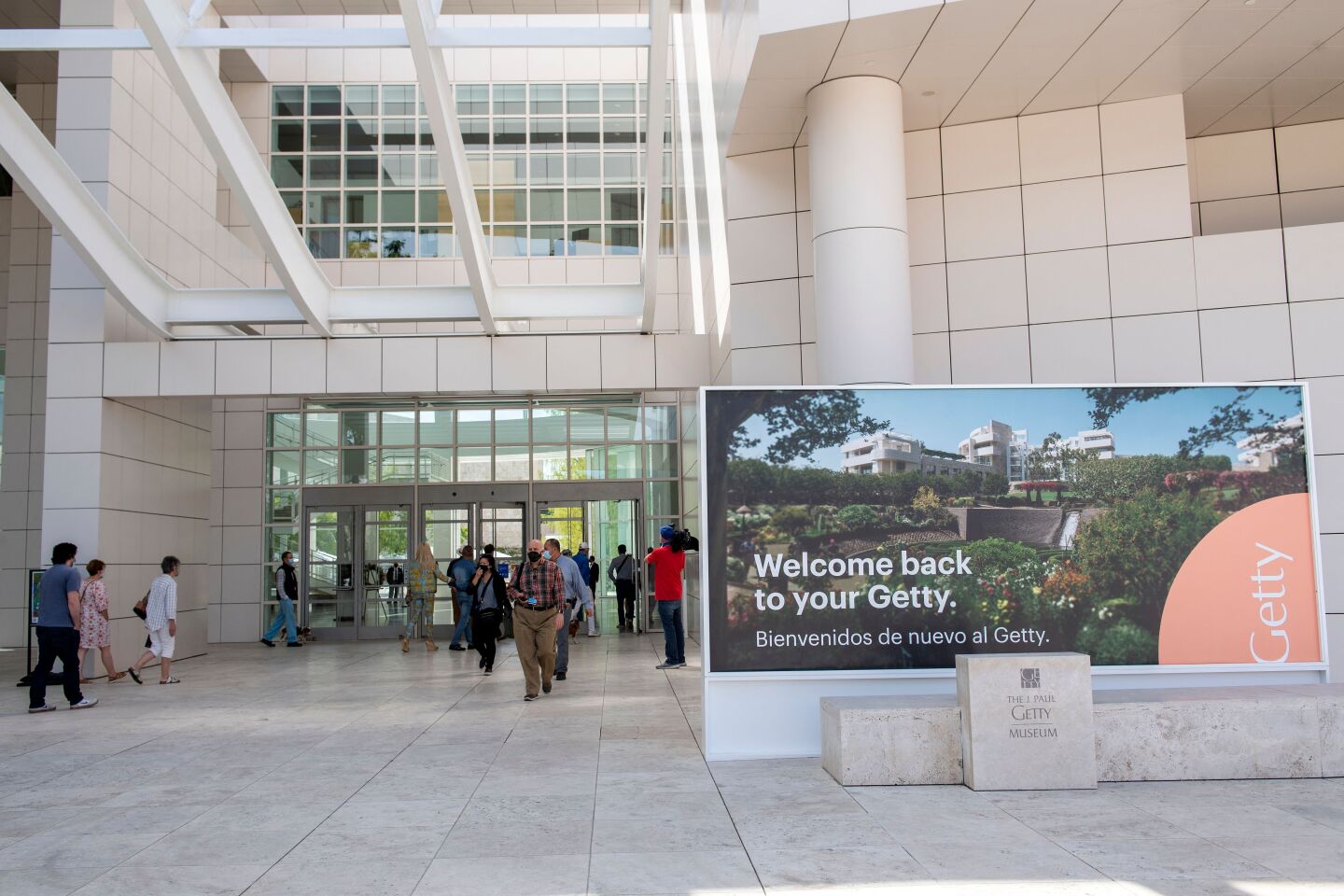The towering entrance to the Getty Museum gas masked people walking in and out of the glass doors and a sign that reads: "Welcome back to your Getty. Bienvenidos de nuevo al Getty."