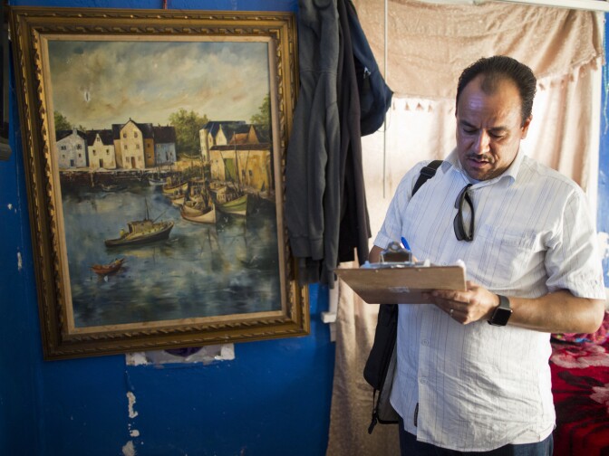 Favian Gonzalez, an organizing coordinator for Strategic Actions for a Just Economy, stands next to a framed painting that covers a foot-wide hole in the wall of an apartment on East Jefferson Boulevard in South Los Angeles.