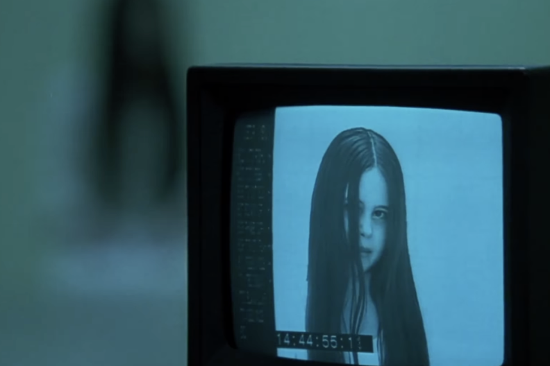 A screenshot of an old monitor showing a young girl with long dark hair from the 2002 film "The Ring."
