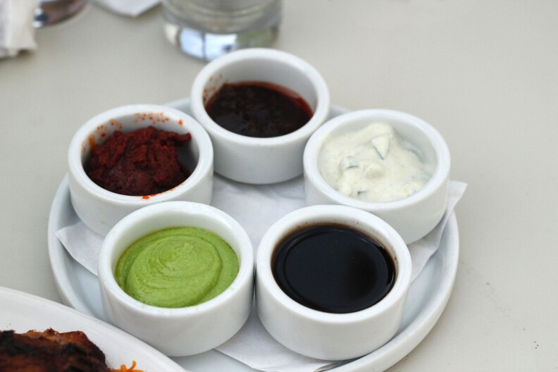 five small white ceramic containers of different sauces sit on a round white tray