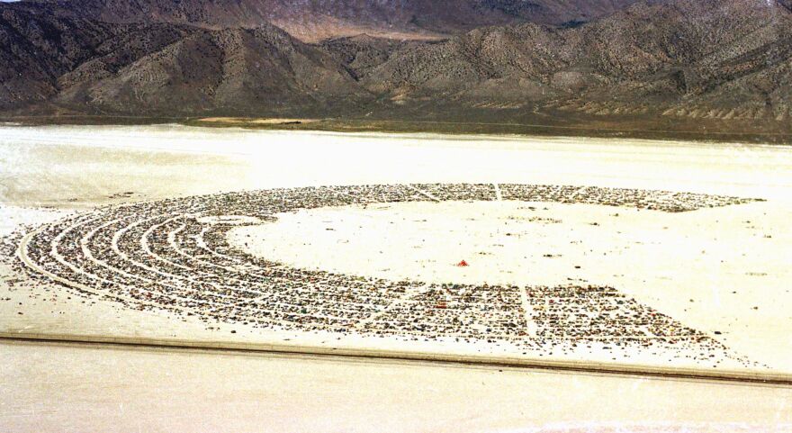 A desert scape has rows and rows of vehicles seen at a distance in a circle that falls short of being complete