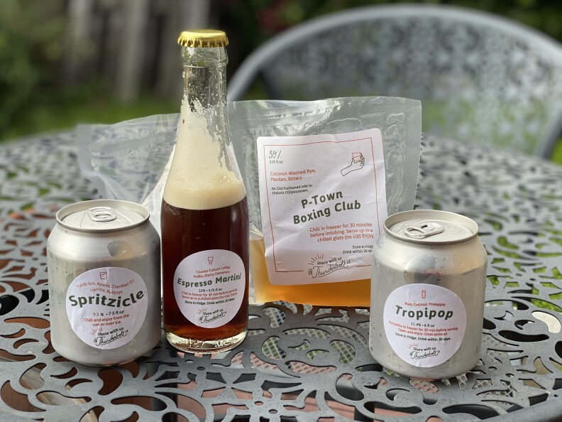 two small aluminum cans, a bottle filled with brown liquid and a bag filled with amber liquid