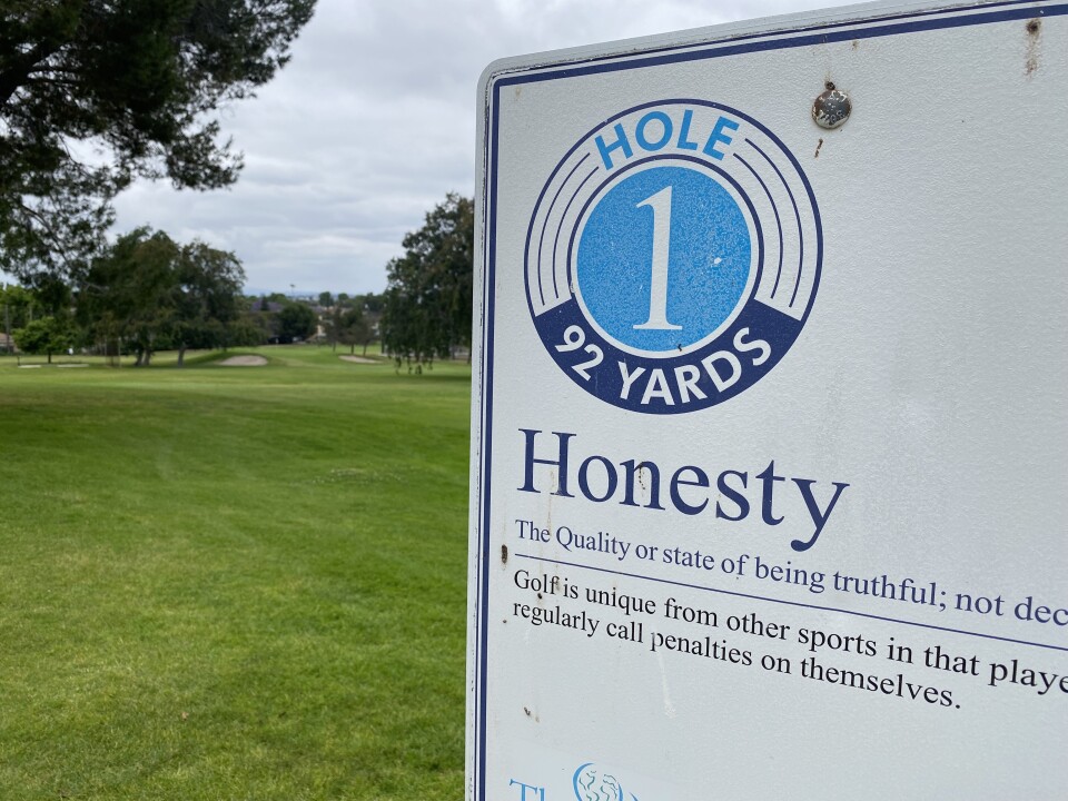 The sign at the first hole of the Maggie Hathaway Golf Course. It says "Hole 1. 92 yards. Honesty. The quality or state of being truthful; not" — then the photo is cut off. The sign also says "Golf is unique from other sports in that played" — here the sign hits the edge of the photo — the next line says "regularly call penalties on themselves."