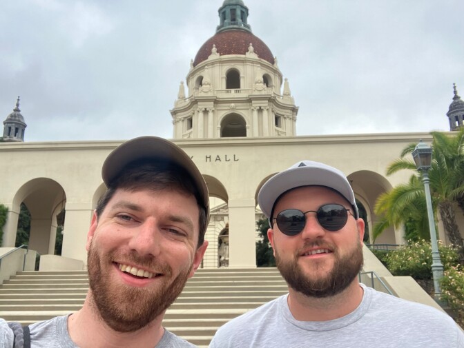 Two men, both wearing hats, post in front of the Pasadena City Hall