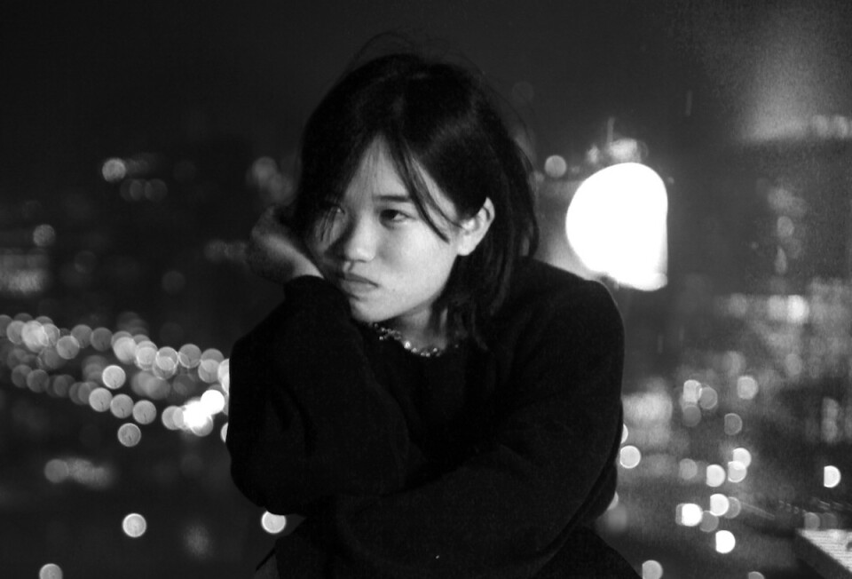 Hana Vu looks pensive against a blurry nighttime skyline. 