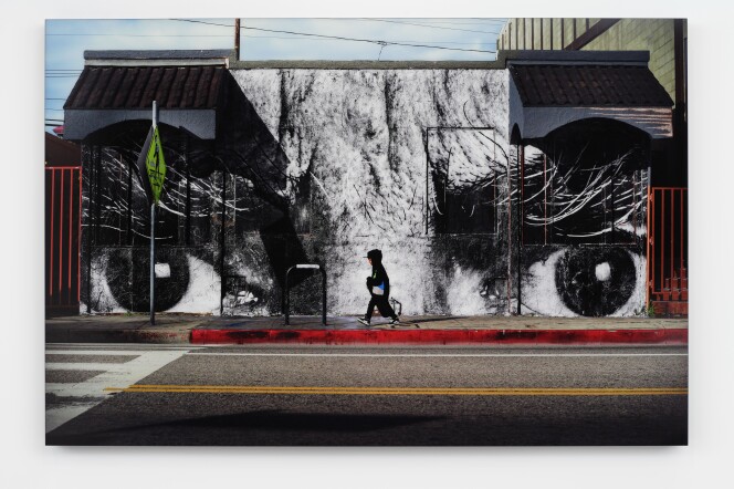 A mural of two large eyes with a person walking on the sidewalk in front of it. 