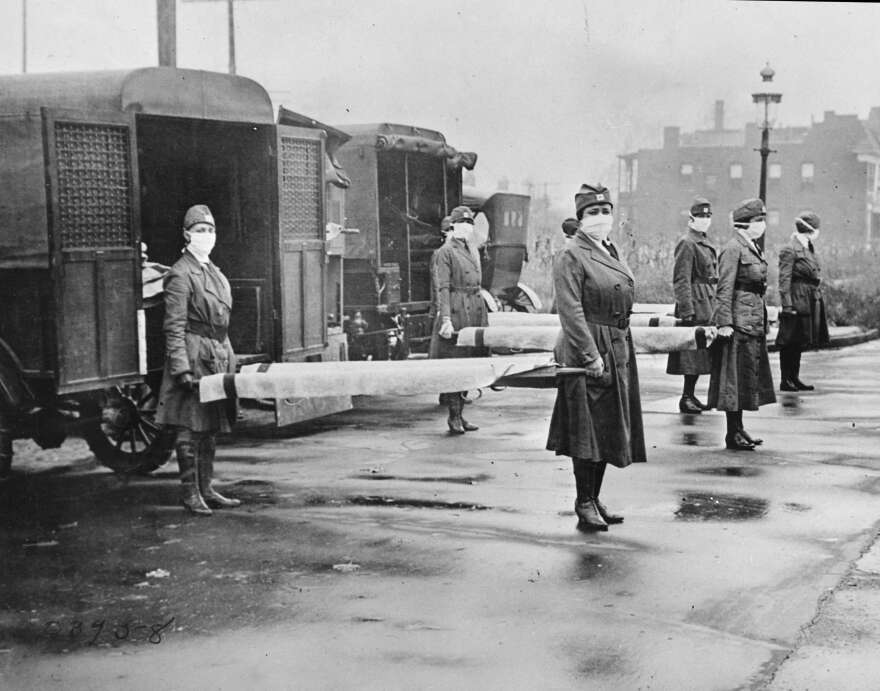 In this October 1918 photo made available by the Library of Congress, St. Louis Red Cross Motor Corps personnel wear masks as they hold stretchers next to ambulances in preparation for victims of the influenza epidemic. (Library of Congress via AP)